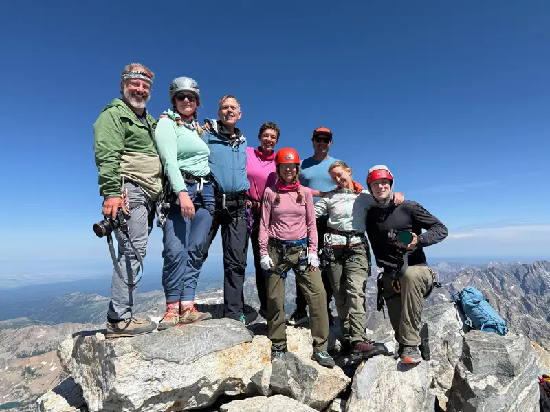 The group of eight standing together on the summit of the Grand Teton under a deep blue sky.
